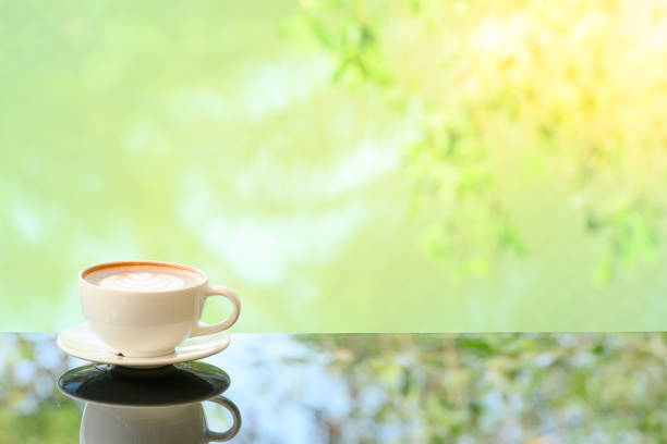 Close-up. Vintage tones Latte art coffee cup on glass table. Blurred leaf reflection background.