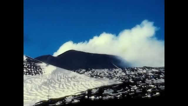 Skiers ride chairlift up towards top of volcano mountain etna