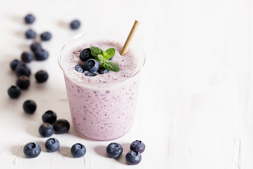 Tasty blueberry smoothie in a glass with pepper straw on white wooden table. Healthy refreshing drink concept.