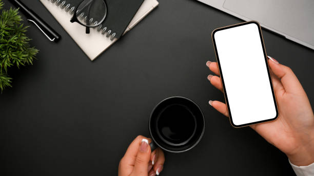 istock Female hand holding smartphone and a coffee cup over modern black desk. 1384108841
