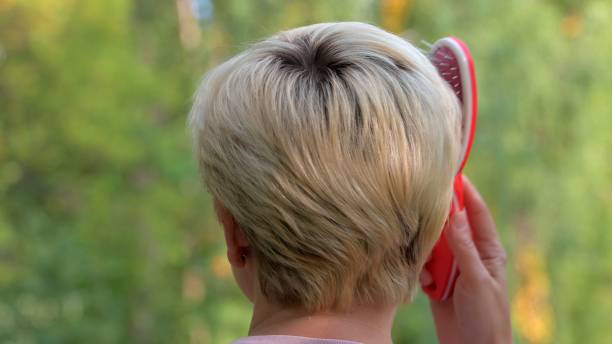 una chica con el pelo corto y rubio se peina el pelo con un peine de masaje rojo sobre el fondo de un primer plano verde de verano - alternative therapy stone zen like nature fotografías e imágenes de stock