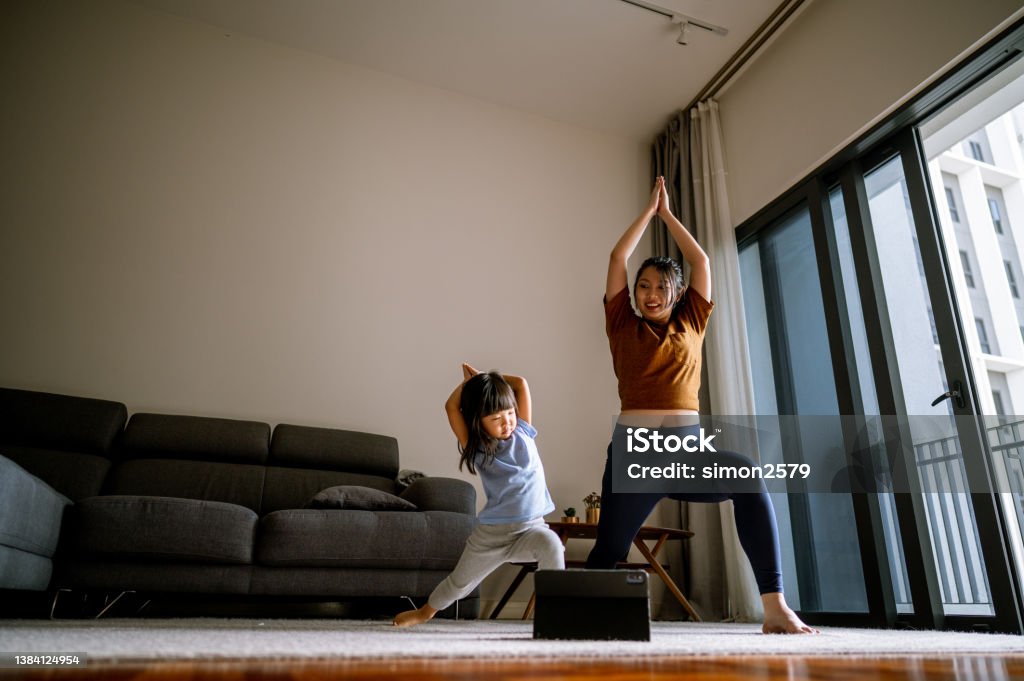 Asian Mother and little girl are doing sport exercises with laptop at home Full length of young Asian woman and her daughter doing fitness together at living room. They are smiling and enjoying workout. Exercising Stock Photo
