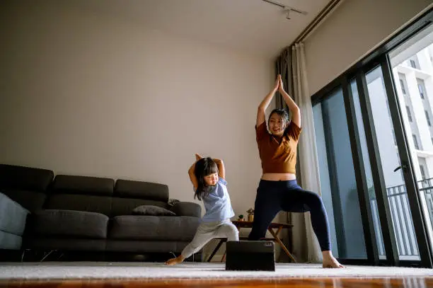 Photo of Asian Mother and little girl are doing sport exercises with laptop at home