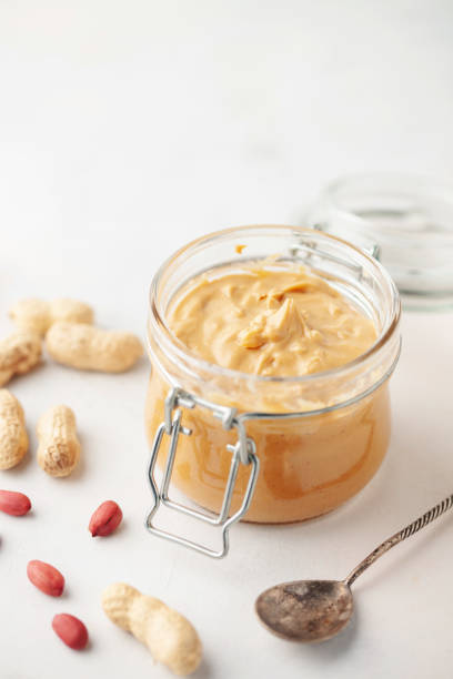 istock Peanut butter or paste jar and heap of nuts on light background. 1384131693
