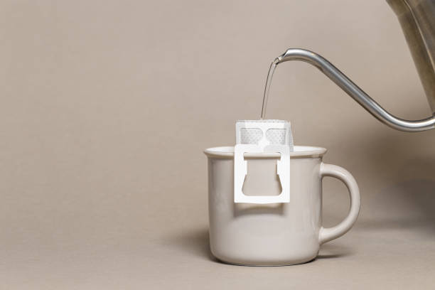 Drip coffee bag with ground coffee in big cup, hot water is poured into paper filter drip coffee for brewing on beige color background, quick way to brew ground coffee