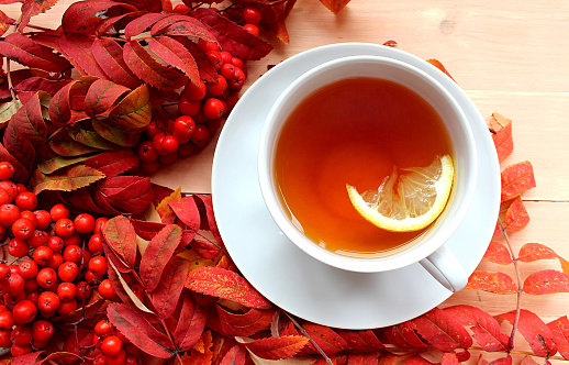 A cup of tea with a piece of lemon on the background of rowanberries on the table.