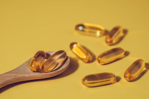 Omega-3 fish oil capsules in the wooden spoon on yellow background Omega-3 fish oil capsules in the wooden spoon on yellow background for healthcare concept Soft Gel stock pictures, royalty-free photos & images