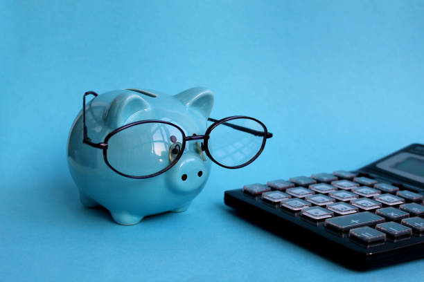 un salvadanaio blu con gli occhiali si trova accanto a una calcolatrice. - spending money foto e immagini stock