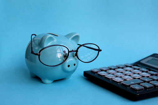 A blue piggy bank with glasses stands next to a calculator.