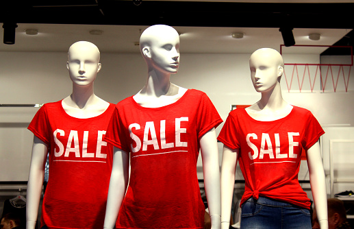There are three mannequins in the store, and the word sale is written on the T-shirts.