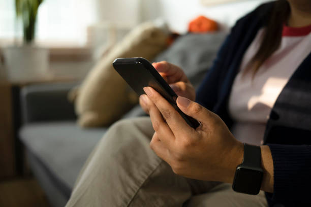istock Cropped short female reading text message on smart phone while sitting on sofa at home. 1384154453