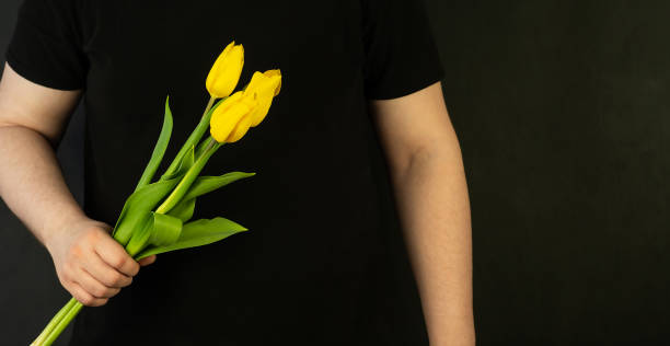 istock A man's hand holds tulips on a black background. 1384155345