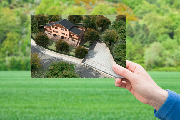 Land plot management - real estate concept with a vacant land on a green residential area available for building construction and hand holding a postcard about a project of a residential building "r"n Land plot management - real estate concept with a vacant land on a green residential area available for building construction and hand holding a postcard about a project of a residential building "r"n empty lot construction stock pictures, royalty-free photos & images