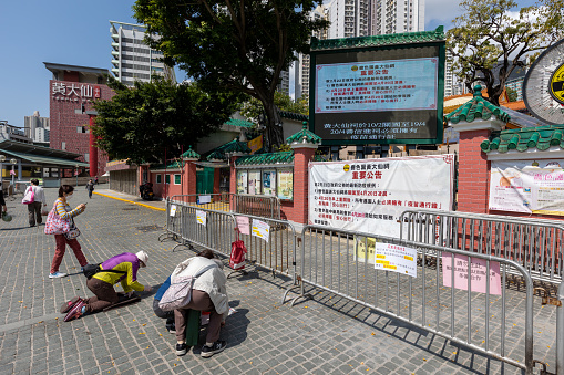 Hong Kong - March 11, 2022 : People praying outside the Wong Tai Sin Temple which is closed due to Covid-19 restrictions in Hong Kong. The Temple will reopen from 20 April 7:30am, and all visitors to the Temple must comply with the relevant requirements under the \