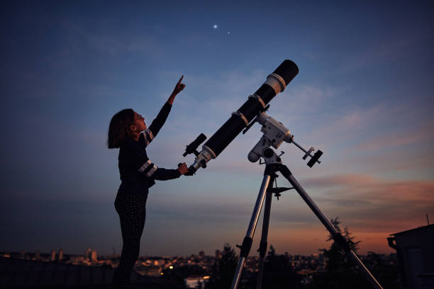 Girl with astronomical telescope stargazing under twilight sky. Girl with astronomical telescope stargazing under twilight sky. telescopic equipment stock pictures, royalty-free photos & images