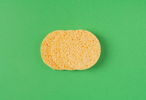 Three round yellow facial sponges on a green background. Skin care accessories. Flat lay, copy space