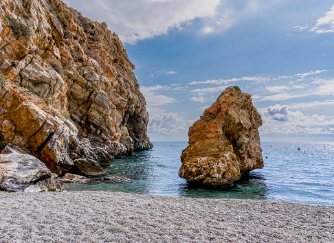A secluded rocky beach with clear turquoise water and brown sandstone cliffs