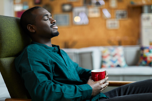 A man sits with a mug of coffee in his hands.