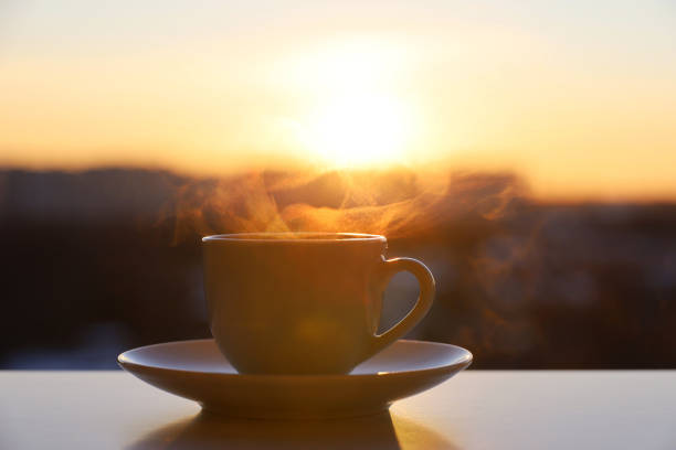 istock Hot coffee or tea cup with smoke on sunset sky background 1384193893