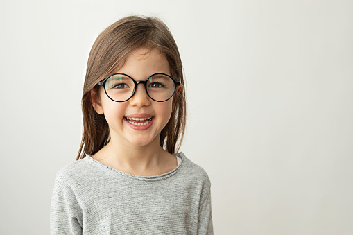Little girl with eyeglasses is smiling at camera.