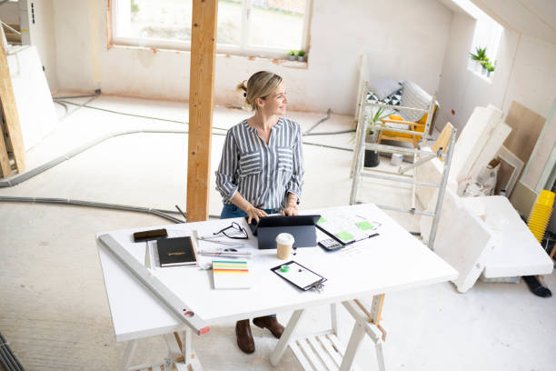 istock pretty young architect working on construction site in a loft and standing by a high table wearing glasses and grey and white striped top 1384206407