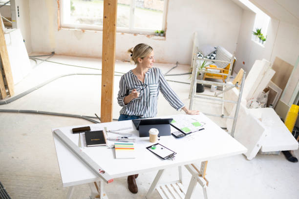 istock pretty young architect working on construction site in a loft and standing by a high table wearing glasses and grey and white striped top 1384207576