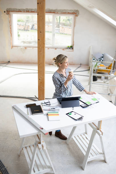 istock pretty young architect working on construction site in a loft and standing by a high table wearing glasses and grey and white striped top 1384207724