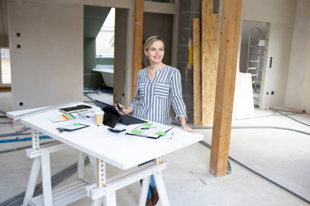 istock pretty young architect working on construction site in a loft and standing by a high table wearing glasses and grey and white striped top 1384207892