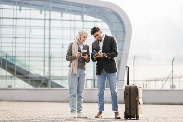 muslim lady in hijab, and arab man, carrying suitcase outside airport, holding passports and tickets - airport business travel arrival departure board travel imagens e fotografias de stock