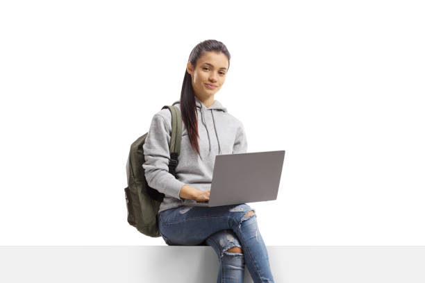 istock Female student with a backpack sitting on a blank panel with a laptop 1384217105