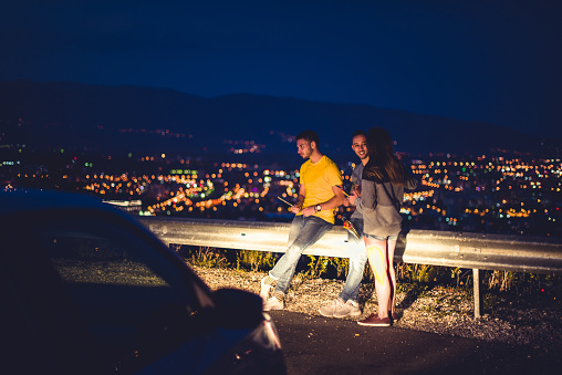 Three people at night are standing and enjoying the city panorama from the road guardrail