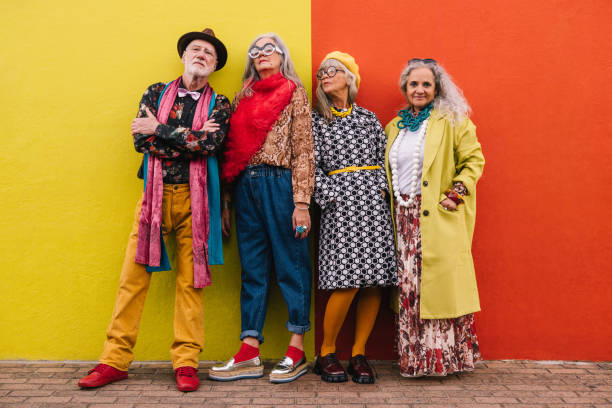 Mature friends standing together against a colourful wall Mature friends looking at the camera while standing together against a colourful wall. Group of four elderly people feeling confident and youthful in colourful clothing. middle aged woman fashion stock pictures, royalty-free photos & images