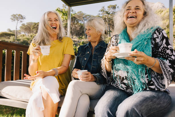 Senior friends laughing happily while having tea Senior women laughing happily while having tea together. Group of elderly friends enjoying their summer vacation at a spa resort. Three mature women enjoying themselves after retirement. baby boomer stock pictures, royalty-free photos & images