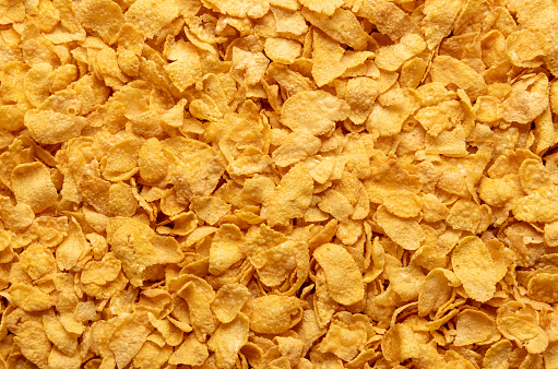 Background full-frame with a pile of cornflakes. Close-up on a myriad of crispy corn cereals view from above. Yellow food background.