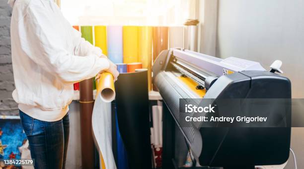 Female Hands Holding Yellow Printable Material On Alarge Format Printing Plotter Graphic Design And Advertising Concept Stock Photo - Download Image Now