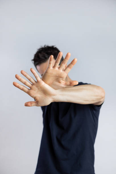 Man covering his face with two hands, Middle age caucasian man, wearing black t-shirt, covering his face with two hands, doing stop gesture. Embarrassed and negative concept. Selective focus on hand, blurred background. Vertical refusing photos stock pictures, royalty-free photos & images