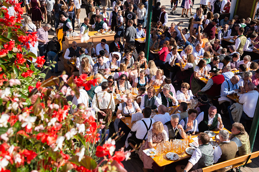 Munich, Germany - September 21, 2019. Crowd sitting at tables and celebrating the Oktoberfest in Munich. The woman wearing typical dirndl and the men lederhosen - the traditional Bavarian clothing. The Oktoberfest is the biggest beer festival of the world with over 6 million visitors each year.