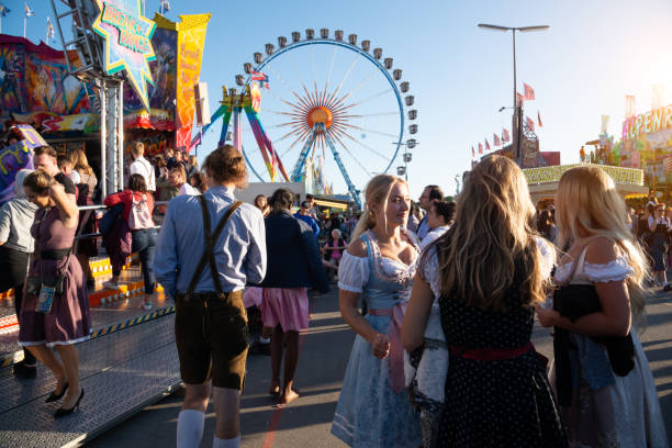 Munich, Germany - September 21, 2019: Visitors Walking through Oktoberfest in Munich, Germany at opening day. The woman wearing typical dirndl and the men lederhosen - the traditional Bavarian clothing. The Oktoberfest is the biggest beer festival of the world with over 6 million visitors each year.