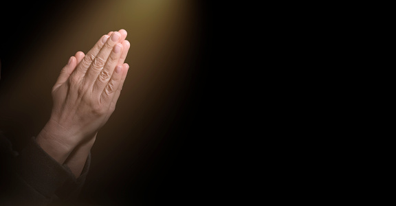 Human Hands Folded in prayer. Praying for faith in religion. Belief in God on dark background. Clasped hands. Power of hope, love and devotion. Namaste gesture. Prayer position. Concept of trust to Christianity. Appeal to heaven, request for donate or forgiveness