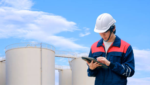 istock Young Asian engineer using digital tablet to working his job with blurred background of storage fuel tanks against cloud on blue sky background 1384232642