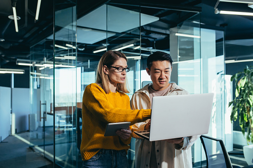 Reunión de negocios de dos empleados, colegas asiáticas y femeninas, discutiendo el proyecto, trabajando en una oficina moderna, mirando la pantalla de una computadora portátil, discutiendo ediciones y el éxito del proyecto. photo