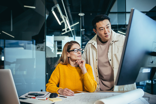 Two freelancers, an Asian man and a woman, work in a modern office, discussing and discussing a joint project, looking at a computer monitor