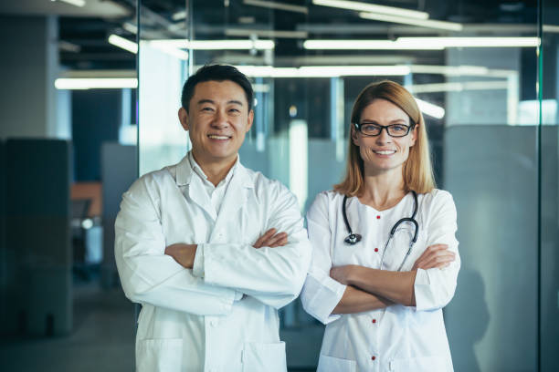 istock Successful and smiling doctors look at the camera and smile, with folded arms, working in a modern clinic, an Asian man and a female team of colleagues 1384233107