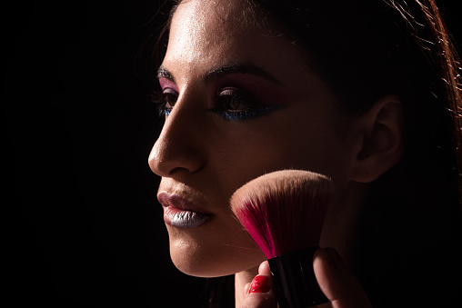 Beautiful young woman applying face powder with brush. Macro shot