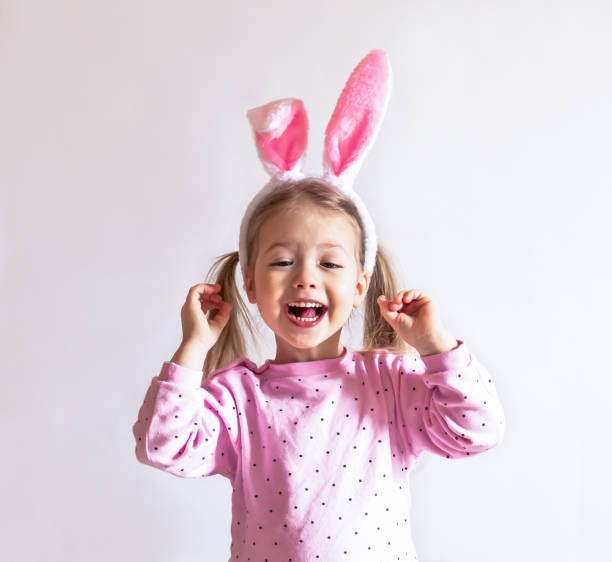 porträt eines süß lächelnden glücklichen kindes in einer rosa jacke mit den osterhasenohren auf hellem hintergrund - bunny girl stock-fotos und bilder