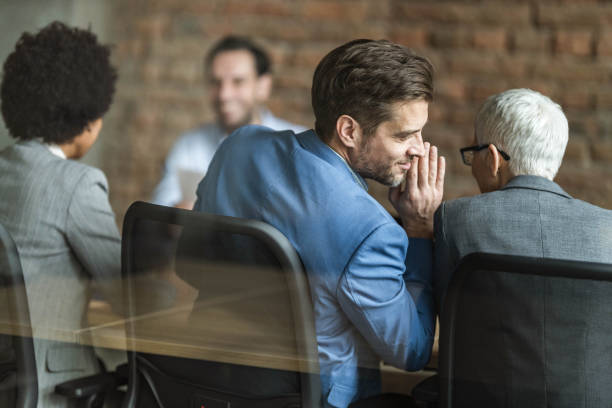 Whispering on a job interview! Back view of male member of human resource team whispering something to his colleague during a job interview in the office. The view is through glass. whispering stock pictures, royalty-free photos & images