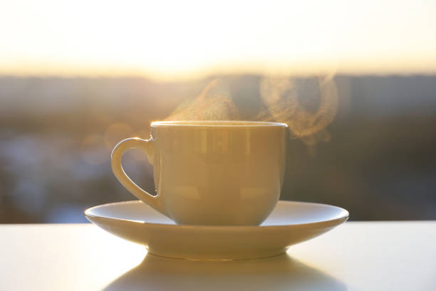 istock Hot coffee or tea cup with steam smoke on shining sun background 1384242576