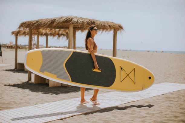young woman with paddle board on the beach on a summer day - women paddleboard bikini surfing imagens e fotografias de stock