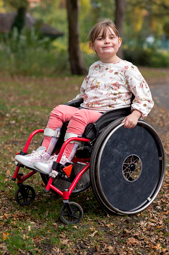 A selective focus front view close up of a young girl sitting in her wheelchair on a beautiful autumn day in a park on a day out with her family in Newcastle upon Tyne in the North East of England.