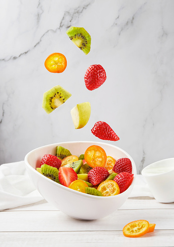 Fresh, healthy, organic fruit salad with flying into the white bowl sliced ingredients on light background. Closeup shot. Levitation